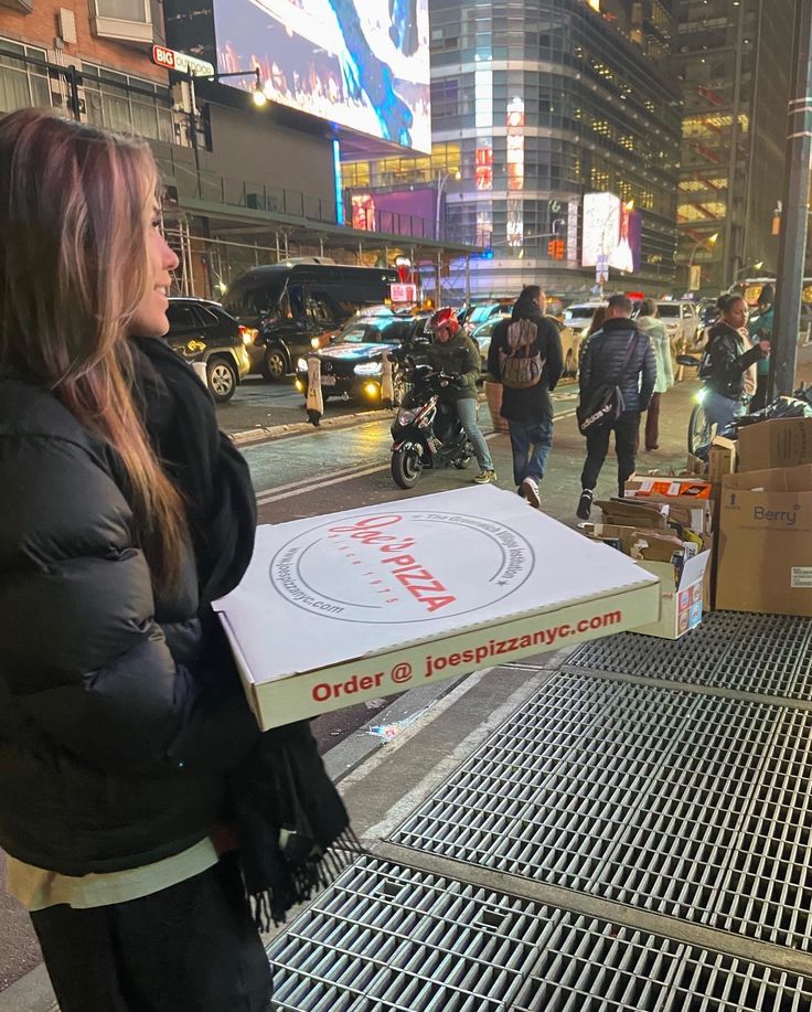 a woman holding a pizza box on the street