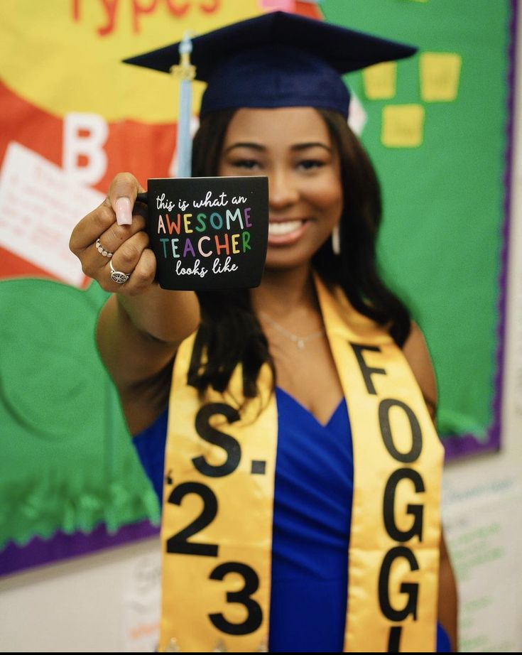 a woman wearing a graduation cap and gown holding up a sign that reads, the teacher is