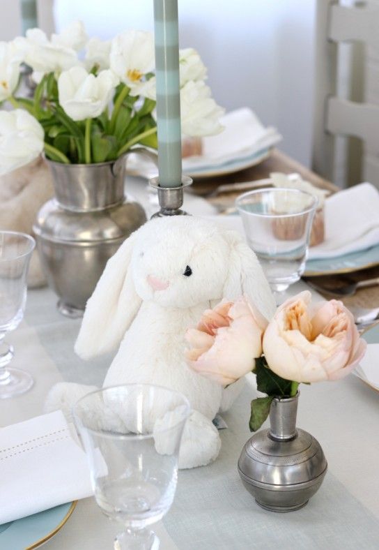 a white bunny sitting on top of a table next to a vase filled with flowers