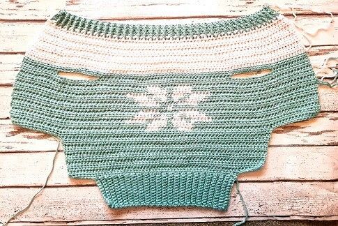 a green and white crocheted sweater sitting on top of a wooden floor