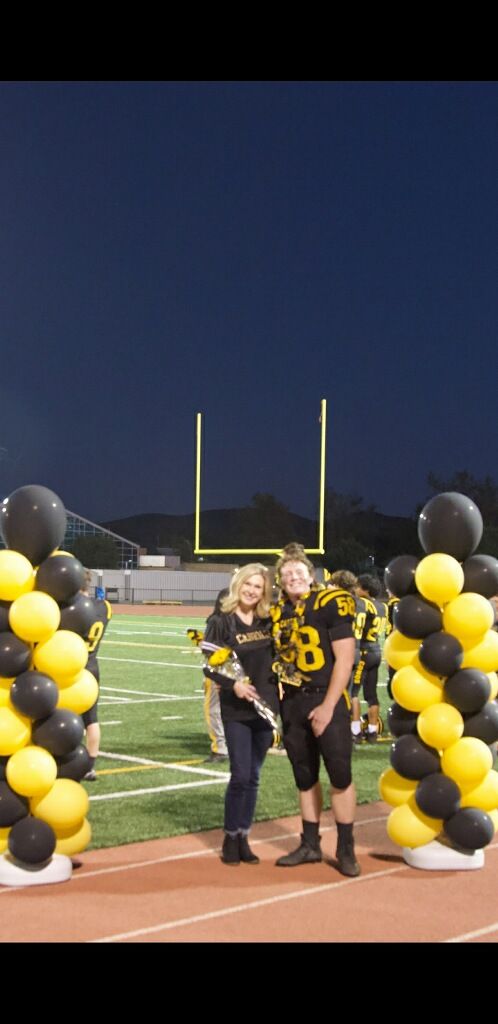 two people standing in front of some black and yellow balloons on a football field at night