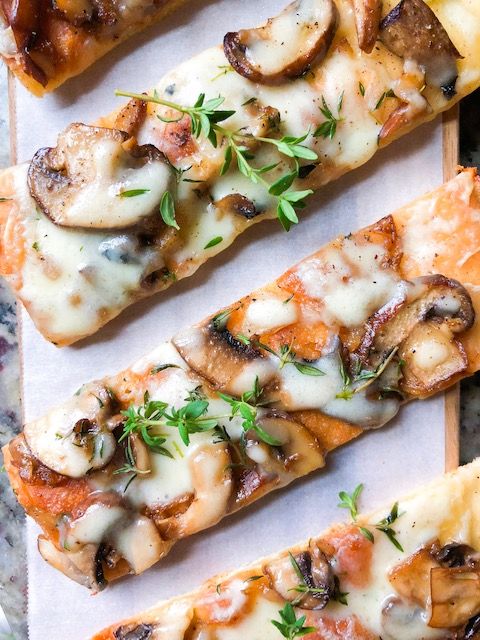 four slices of pizza with mushrooms, cheese and herbs on them sitting on a cutting board