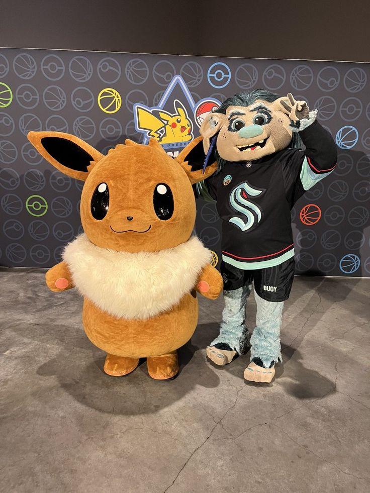 two people in costume standing next to each other near a wall with pokemon characters on it