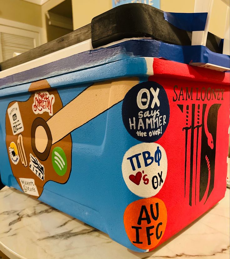 a blue and red cooler with stickers on it's lid sitting on a counter