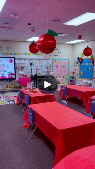 an empty classroom with red tables and pink tablecloths on the walls, and large television in the background