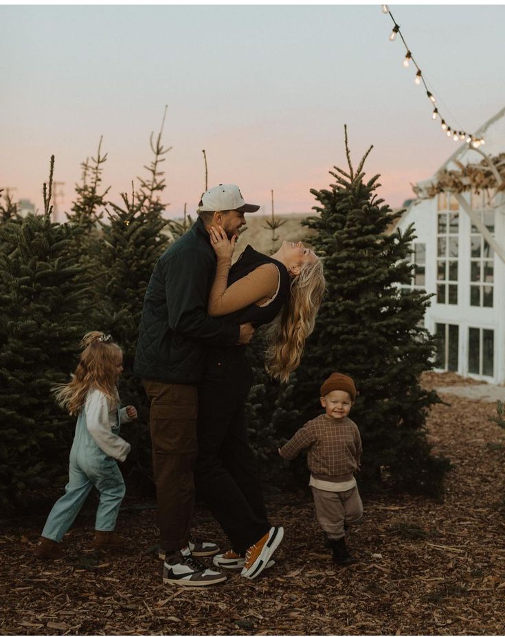 a man and woman kissing in front of christmas trees with two children on the ground