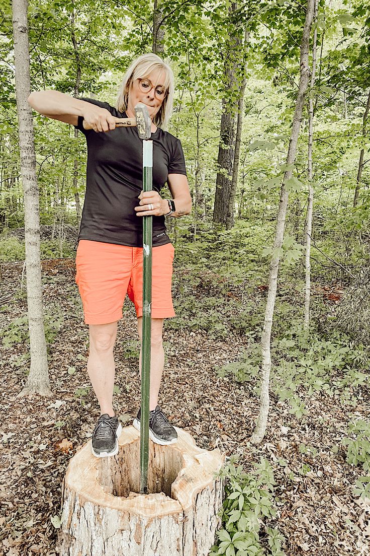 a woman standing on top of a tree stump holding onto a wooden pole in the woods