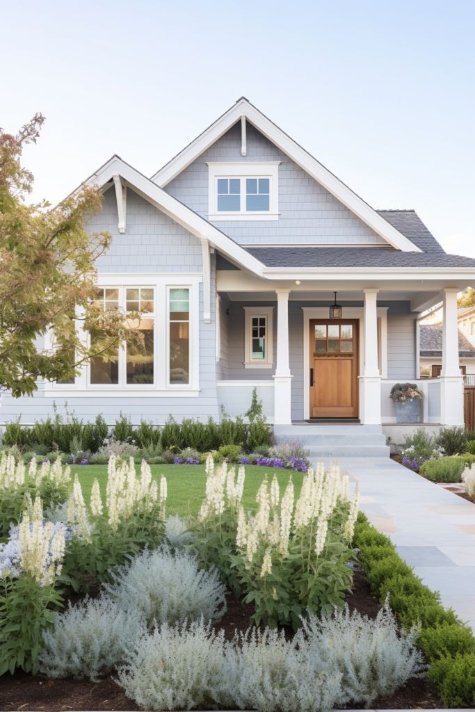 a gray house with white trim and flowers in the front yard, along with lavender bushes