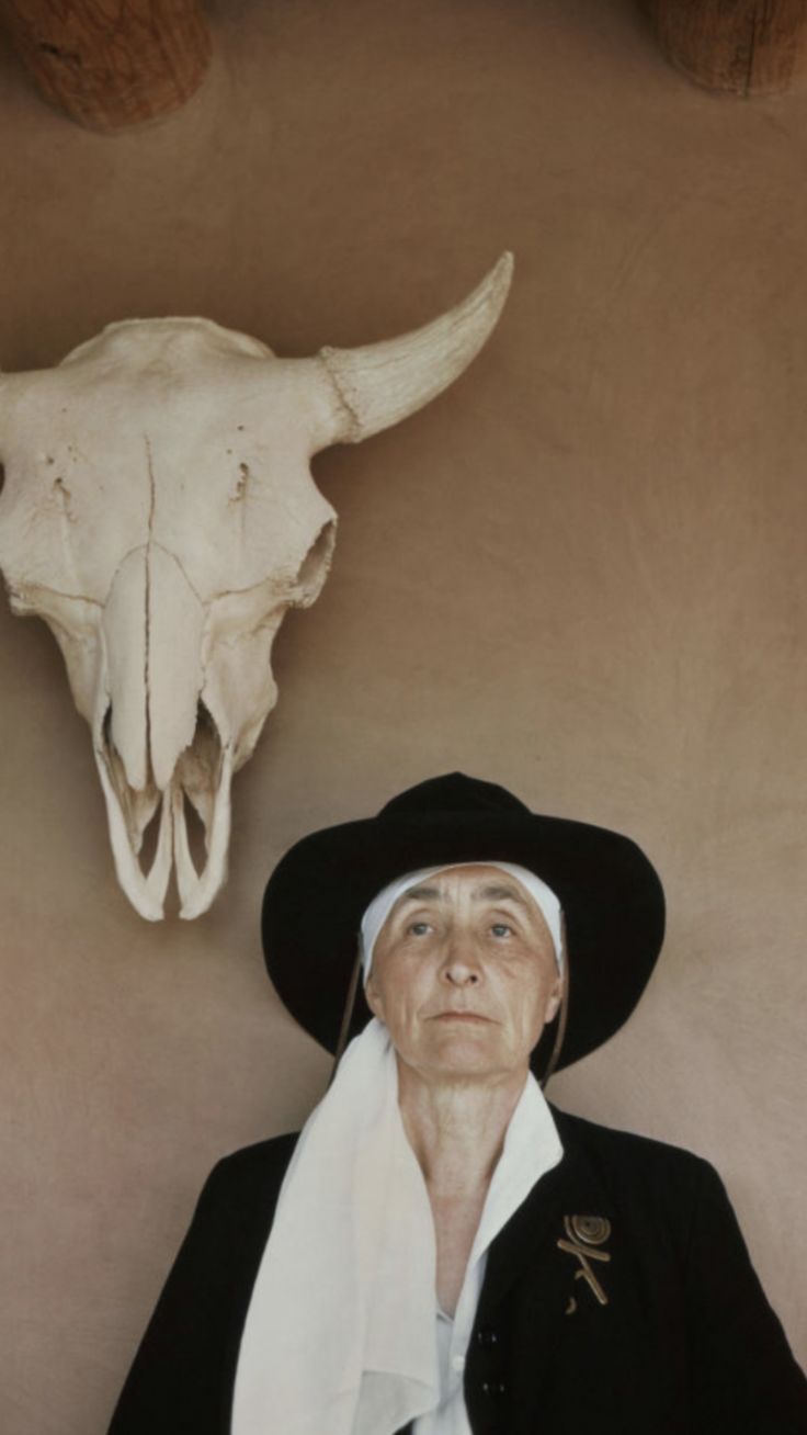 a man wearing a black hat standing next to a white cow skull on the wall