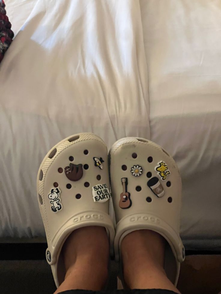 someone's feet wearing crocs with stickers on them in front of a bed