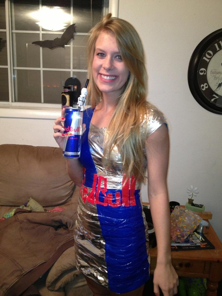 a woman in a silver and blue dress is holding a can of beer while standing next to a couch