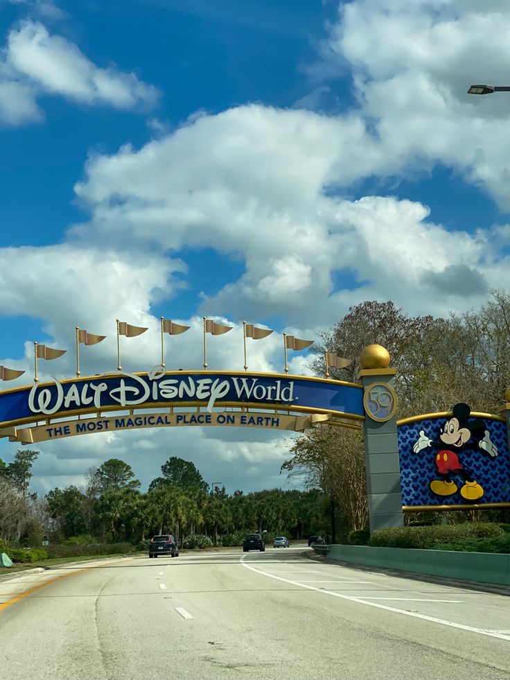 the entrance to walt world with cars driving under it and flags flying in the air