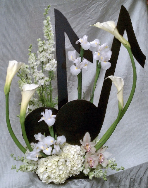 a vase filled with white flowers on top of a bed next to a black letter