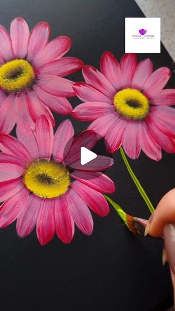 someone is painting pink flowers on a black surface with yellow centers and the petals are being painted