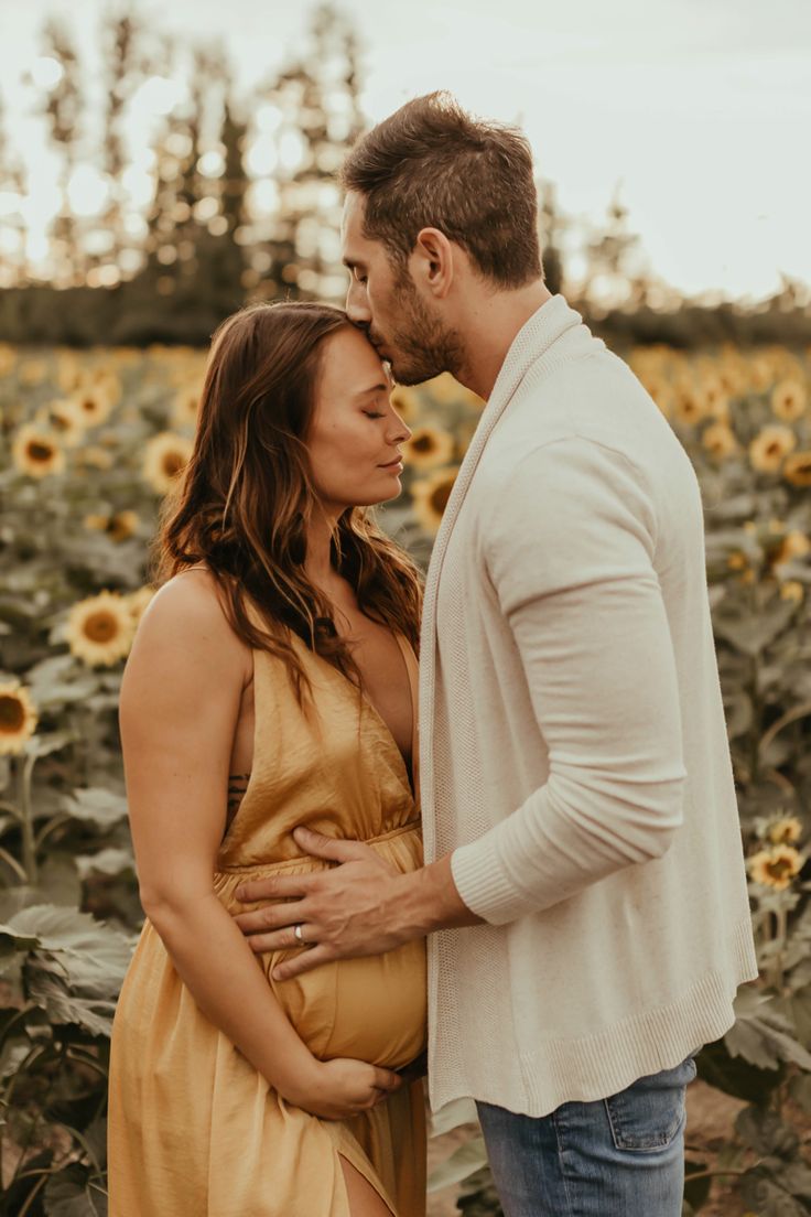 a pregnant couple standing in front of a sunflower field