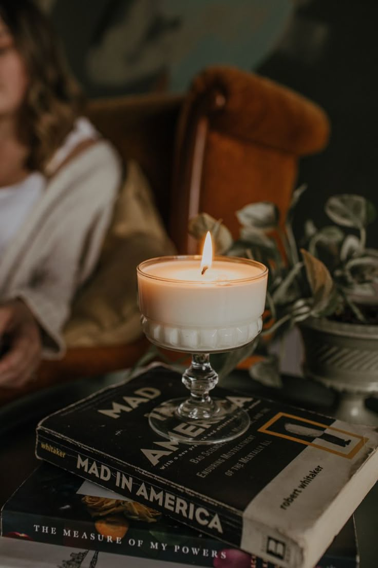 a candle sitting on top of a stack of books next to a woman in a chair