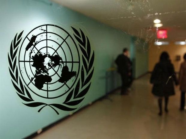 people walk past the united nations logo in an airport