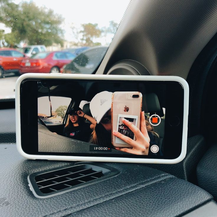 a person taking a selfie in the car with their cell phone on the dashboard