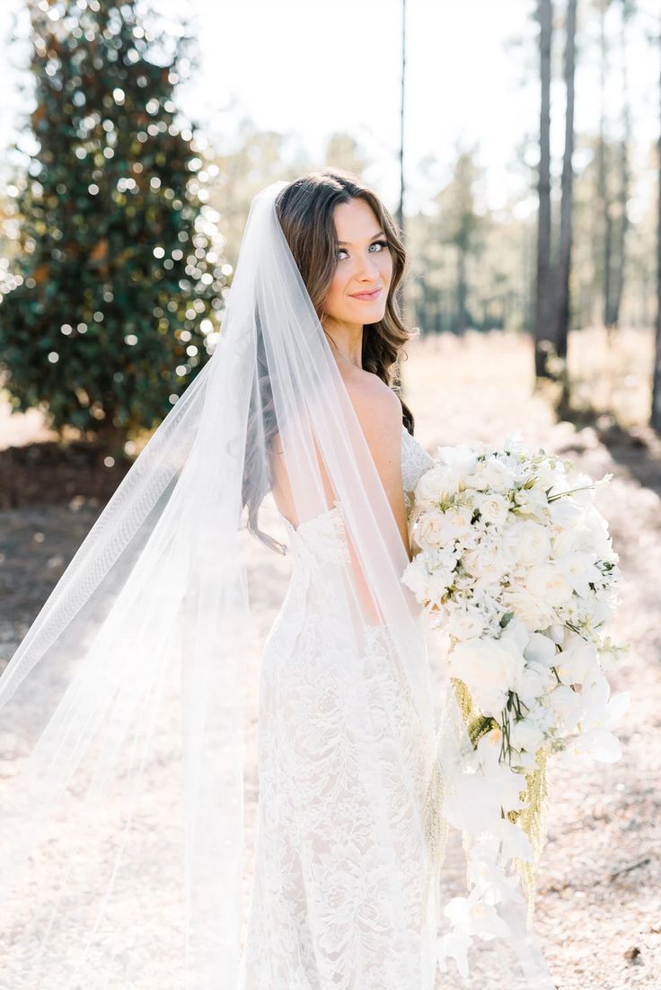 a woman in a wedding dress holding a bouquet of flowers and a veil over her head