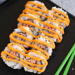 sushi rolls with orange sauce and chopsticks on a black plate next to green onions