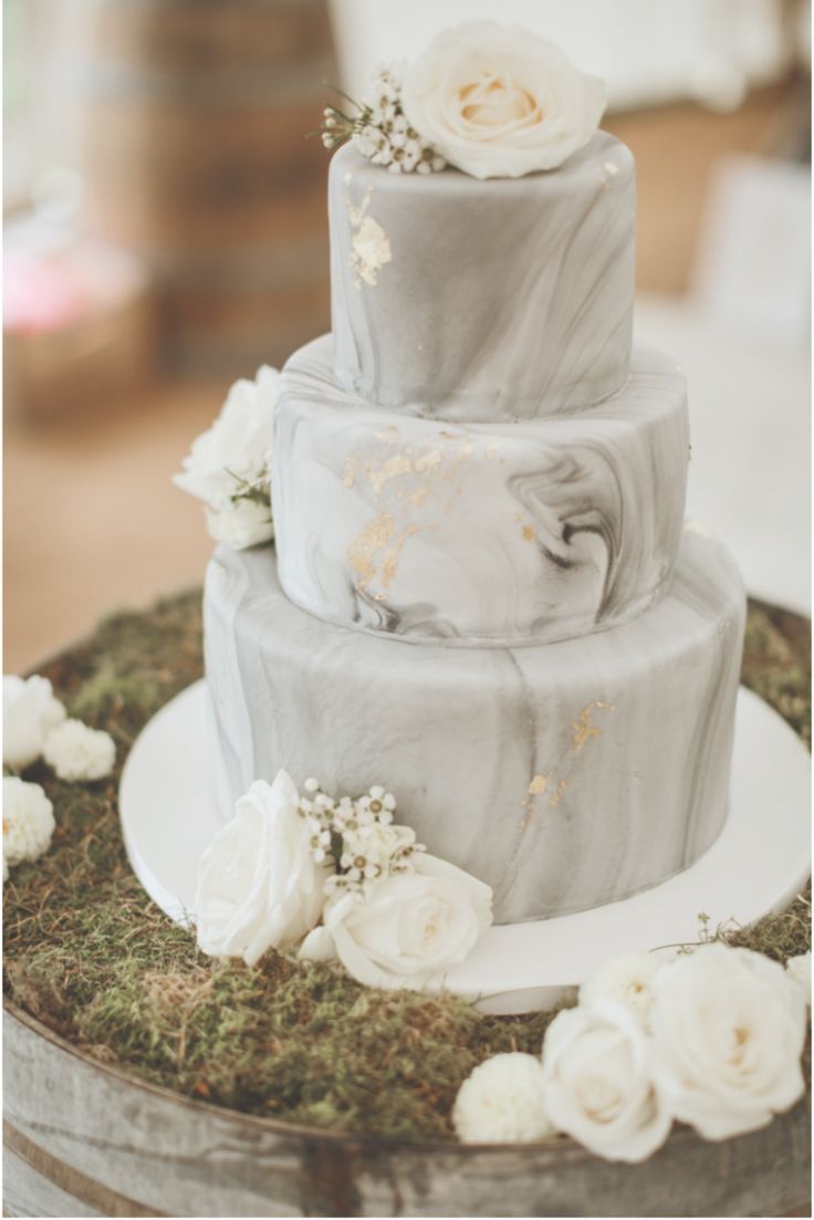 a three tiered wedding cake with white flowers on the top and green moss growing around it