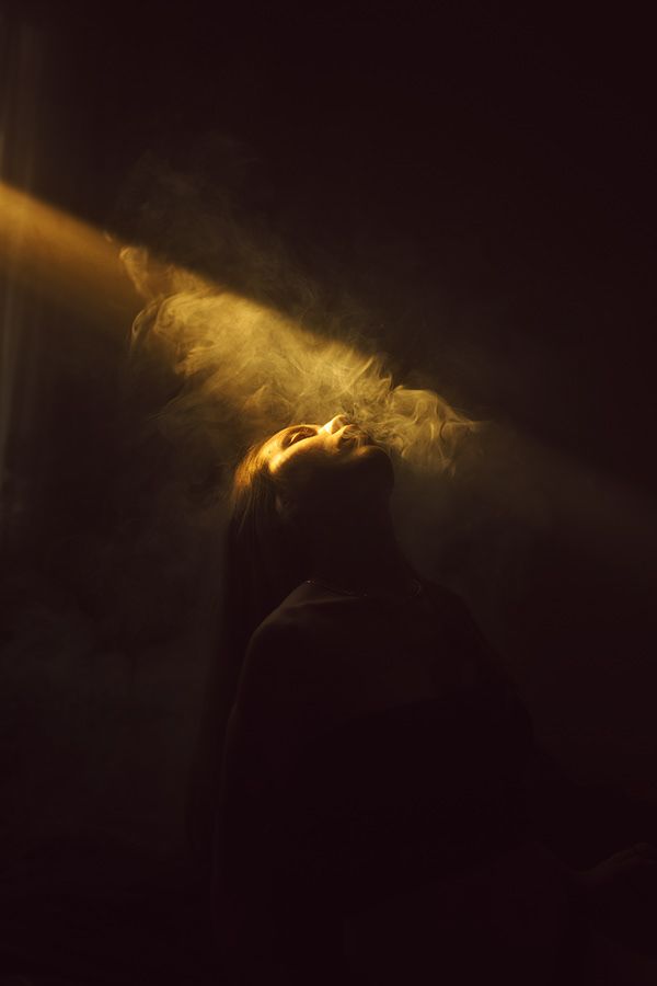 a woman standing in the dark with her eyes closed and light coming from behind her