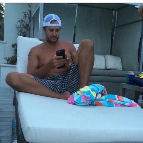 a man sitting on top of a white couch next to a pool holding a cell phone