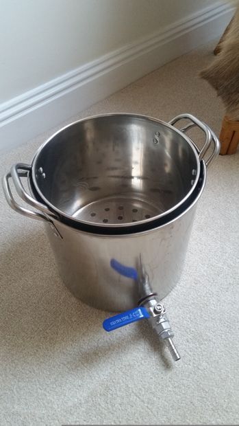 a large stainless steel pot sitting on the floor next to a blue handled spatula