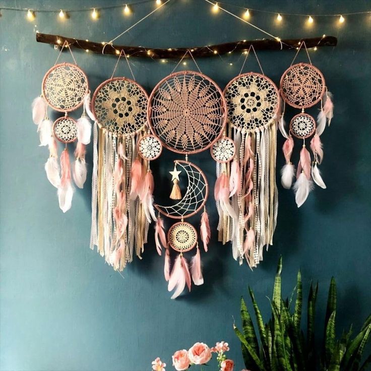 a wall hanging with dream catchers and lights in the corner next to a potted plant