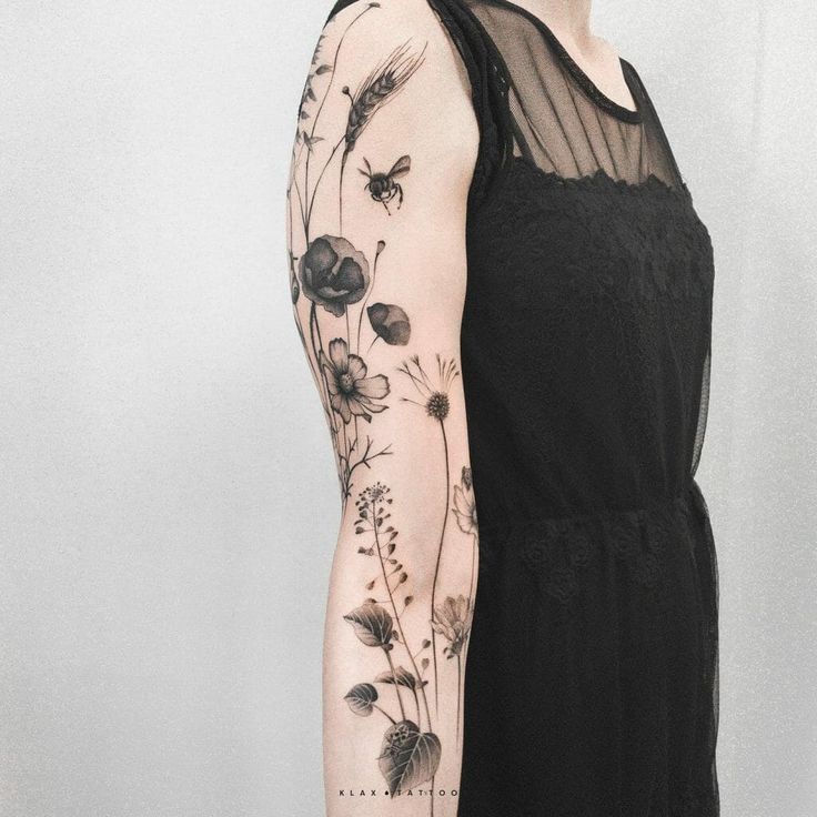 a woman wearing a black dress with flowers on her arm and tattoos on her arms