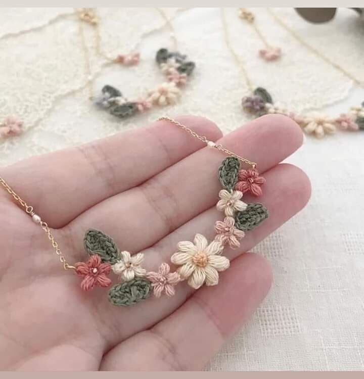 a hand holding a necklace with flowers on it