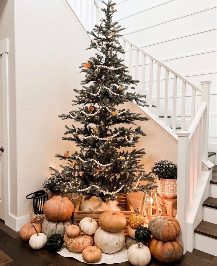 a christmas tree is surrounded by pumpkins and other decorations on the floor in front of a staircase