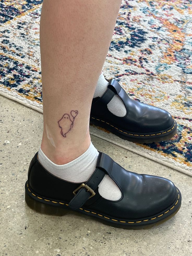 a person with a small tattoo on their foot wearing black clogs and white socks