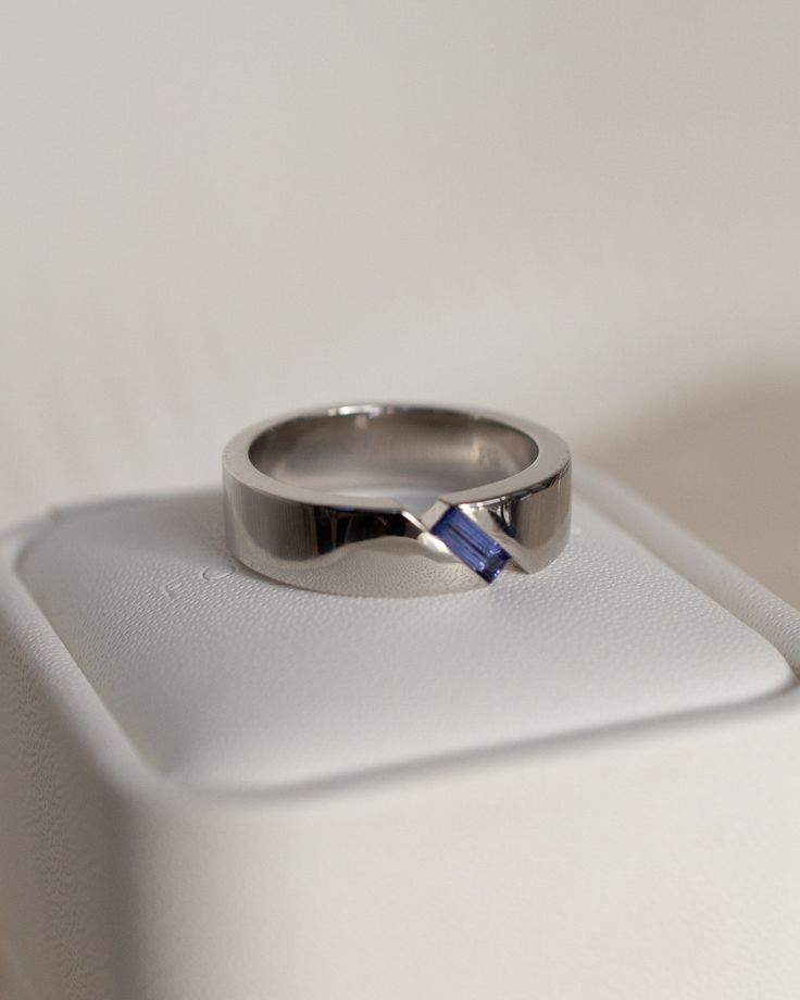 a wedding ring with a blue stone in the center on a white surface, close up