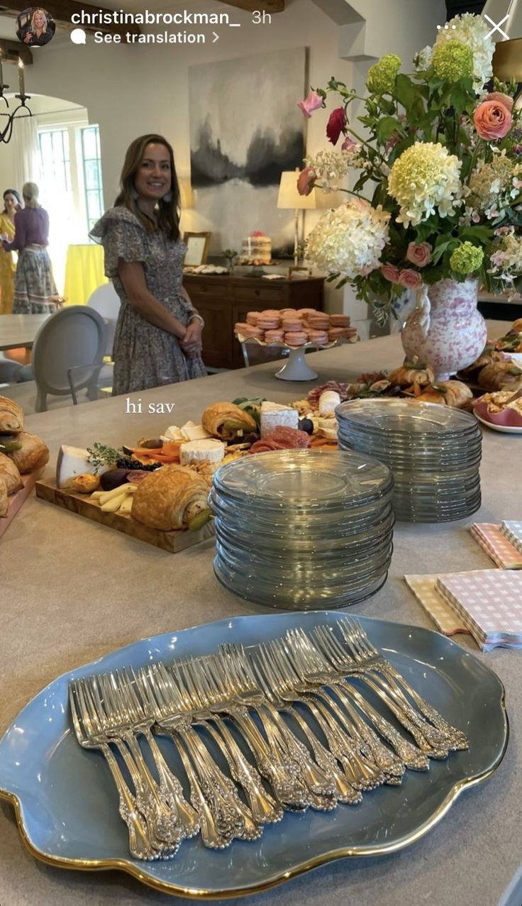 a woman standing in front of a table filled with plates and silver utensils