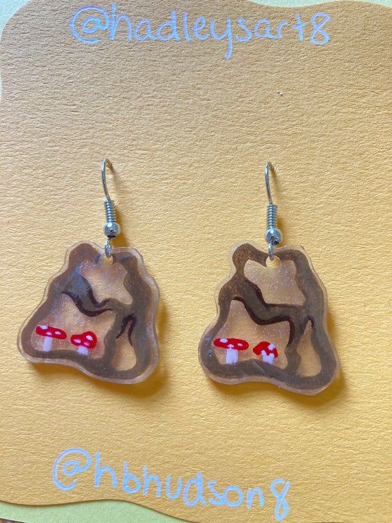 the earrings are made out of clay and have red mushrooms on them, with words underneath