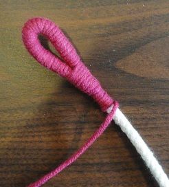 a close up of a pink and white object on a wooden table with yarn in it