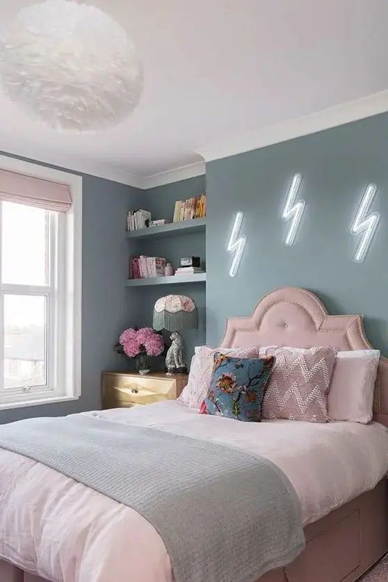 a bedroom with blue walls, pink bedding and white pillows on the headboard