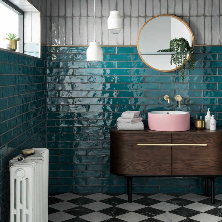 a bathroom with green tiles and a round mirror on the wall next to a sink