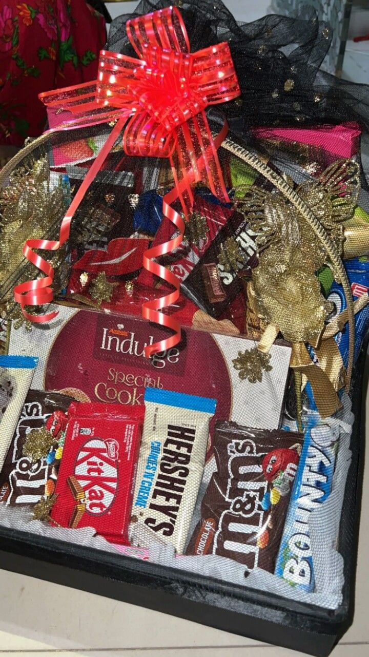 an assortment of chocolates and candy in a gift basket with ribbons on the top