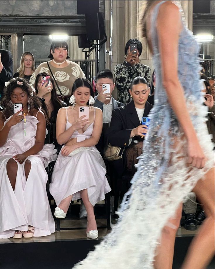 several models are taking pictures with their cell phones at the fashion show in front of an audience