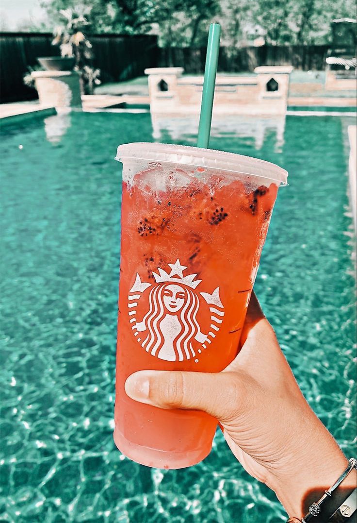 a person holding up a drink in front of a swimming pool