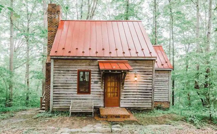 an old log cabin in the woods with a red tin roof and metal shingles