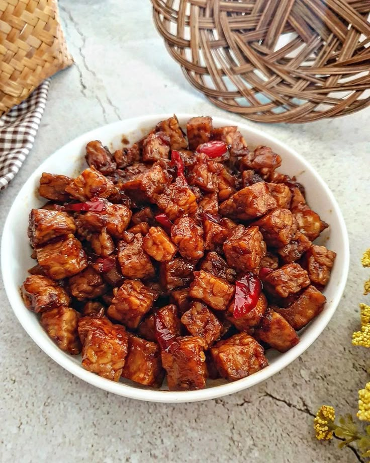 a white bowl filled with meat sitting on top of a table next to yellow flowers