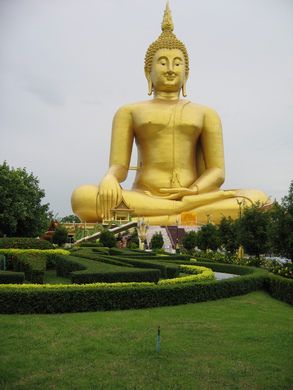 a large golden buddha statue sitting in the middle of a lush green park with hedges