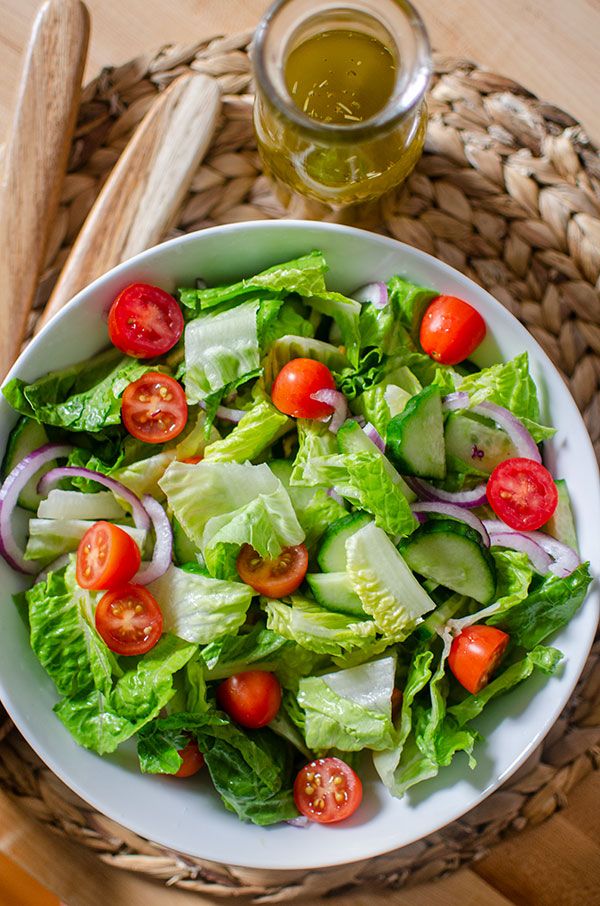 a white bowl filled with lettuce and tomatoes next to a glass of olive oil