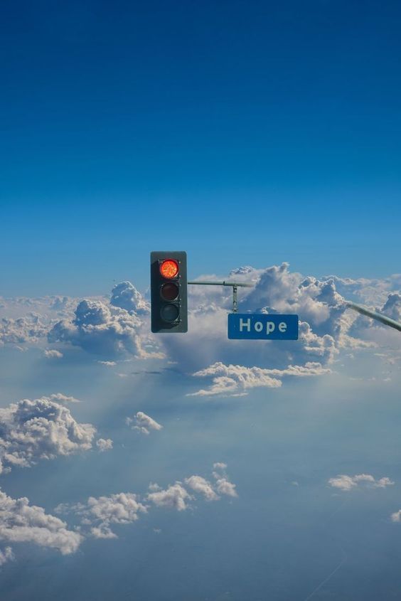 a traffic light above the clouds with hope sign in foreground and blue sky behind it