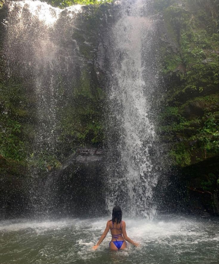 a woman is in the water near a waterfall