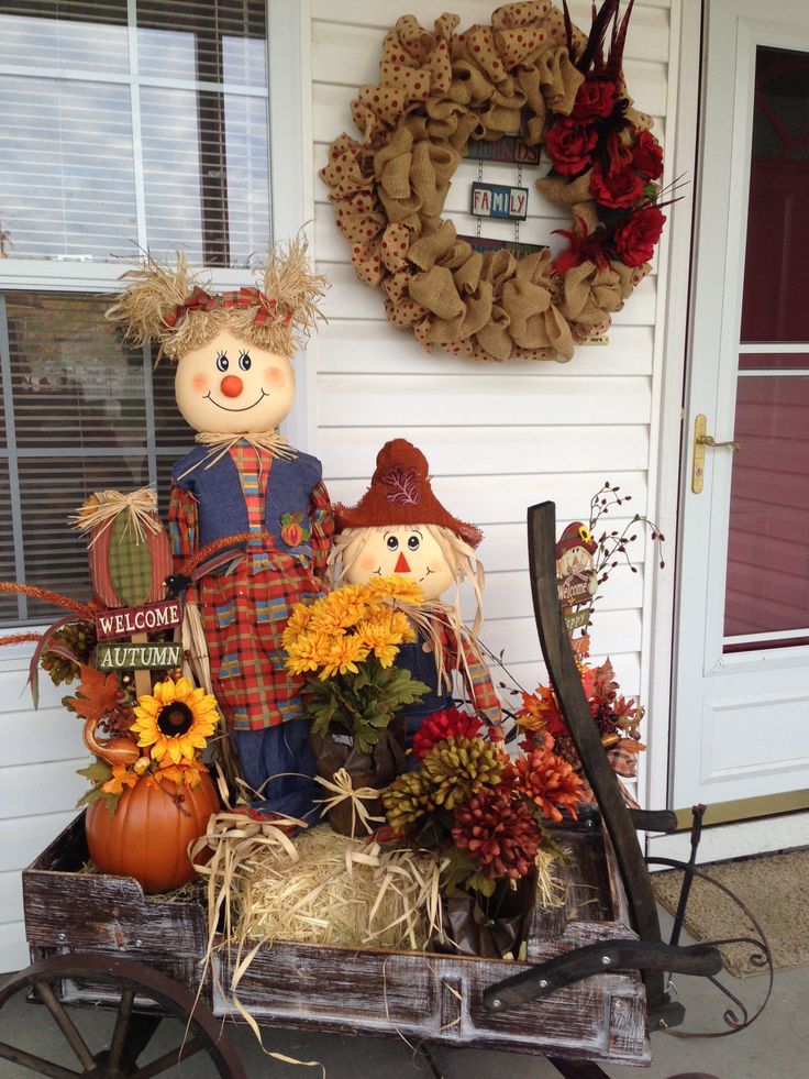 two scarecrows sitting on top of a wagon filled with flowers and pumpkins