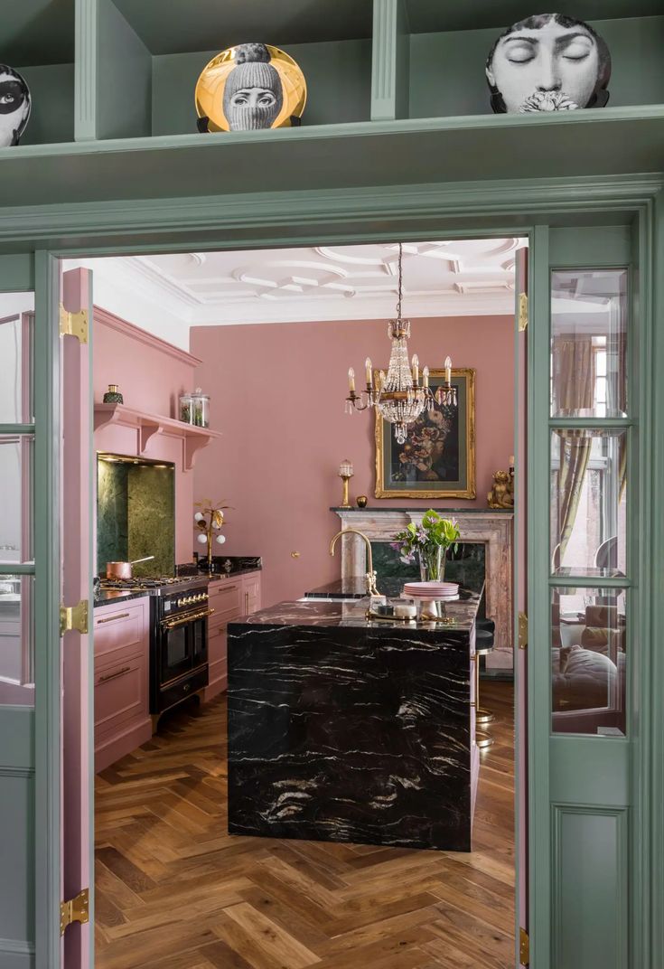 an open door leading to a kitchen with pink walls and wood floors, chandelier hanging from the ceiling